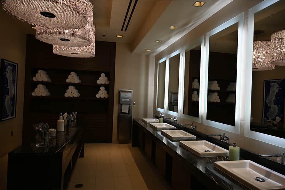 Luxury bathroom with multiple sinks, lighted mirrors, and decorative towel storage