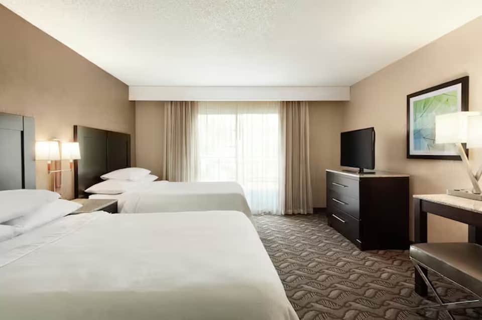 Hotel room with two queen beds, neutral tones, and sliding glass door to balcony