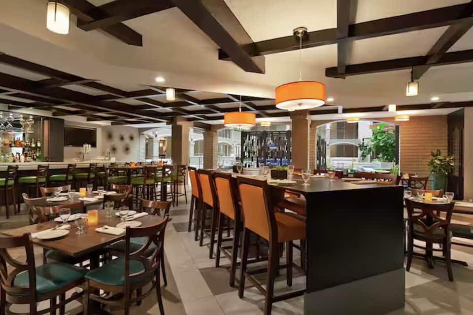 Modern restaurant interior with wooden tables, orange pendant lights, and bar seating