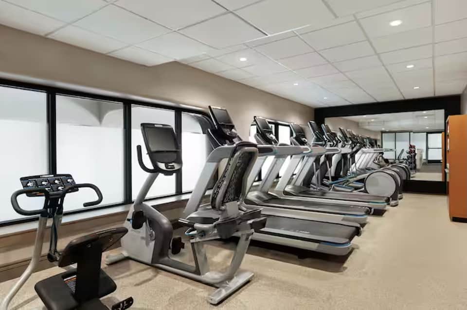 Bright fitness center with multiple treadmills, recumbent bikes, and windows overlooking the city