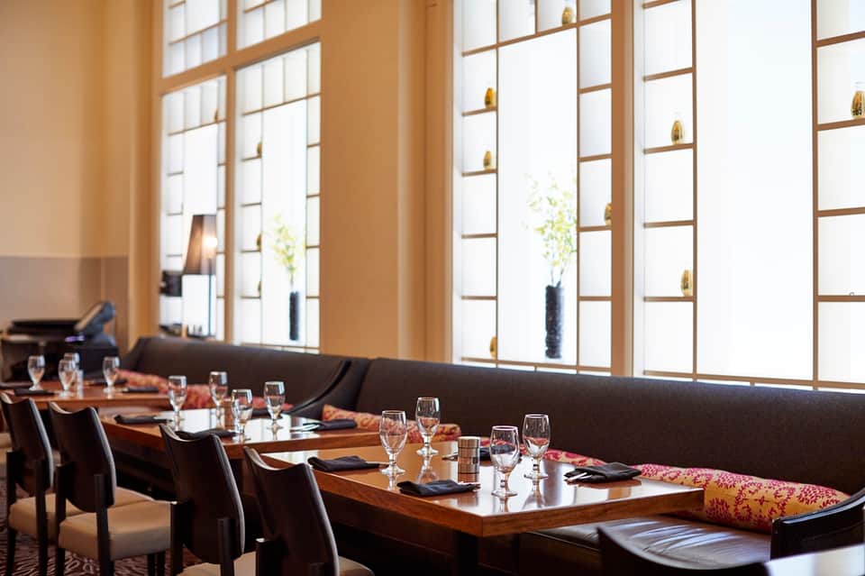 Upscale restaurant dining room with wooden tables, dark chairs, and floor-to-ceiling windows