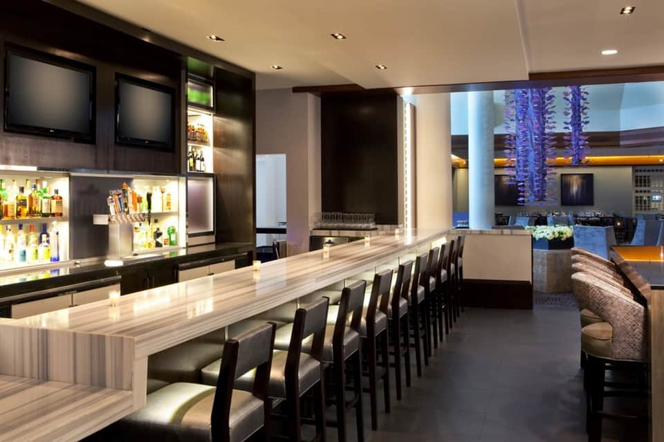 Upscale bar interior with light wood counter, black seating, and ambient lighting