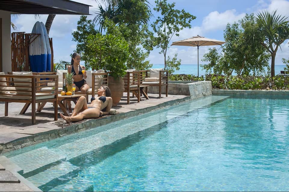 Tropical pool deck with lounge chairs, ocean view, umbrellas, and beachfront vegetation