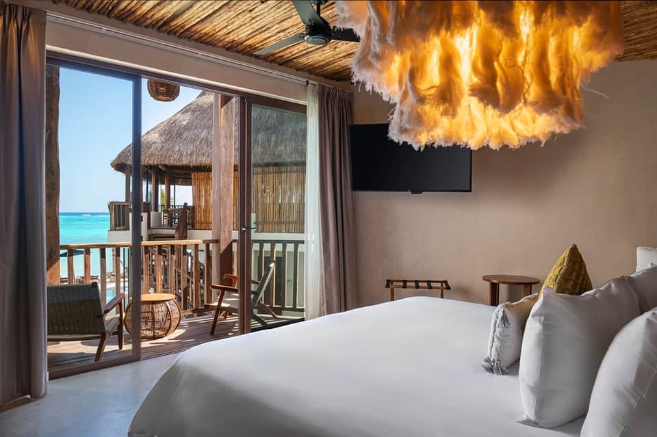 Overwater bungalow bedroom with ocean view, balcony, and tropical decor