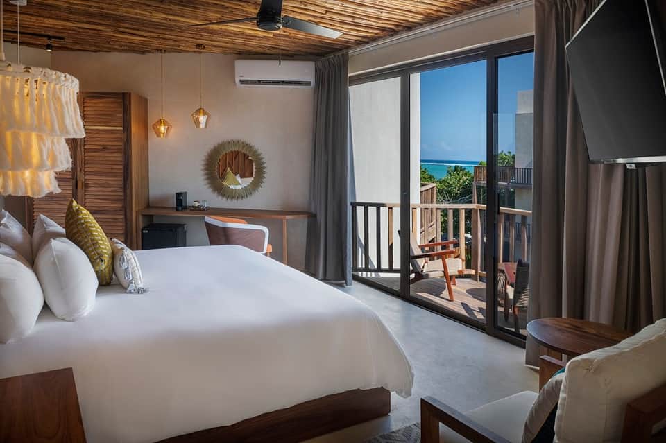 Beachfront hotel room with king bed, ocean view from balcony, modern furnishings, and natural light