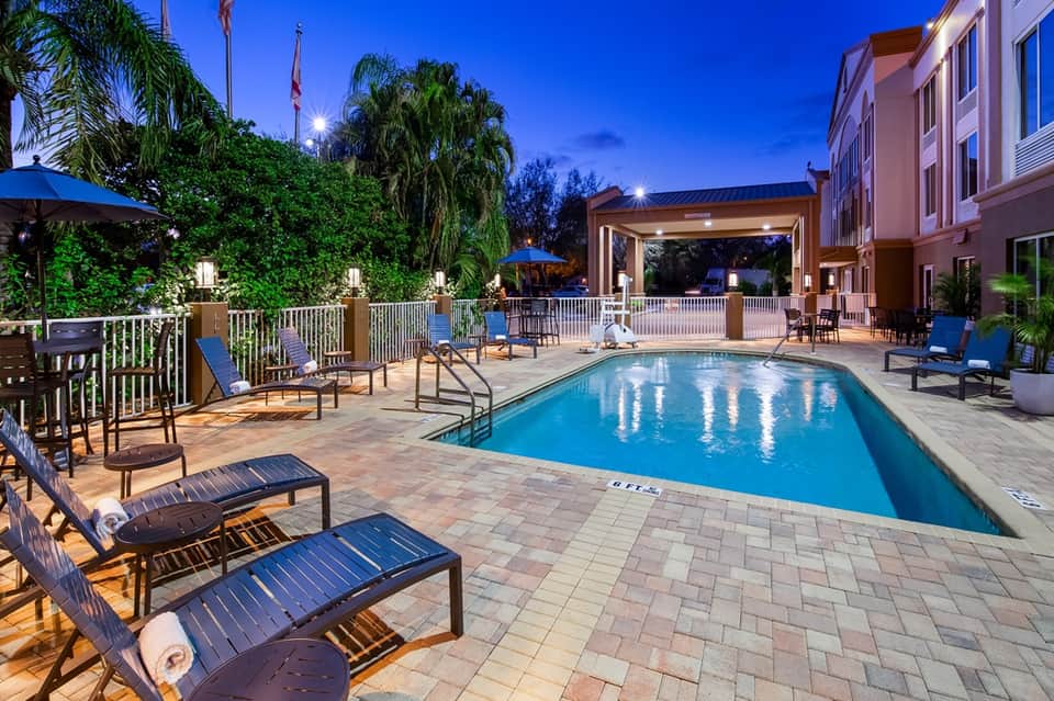 Resort pool at night with illuminated deck, lounge chairs, and palm trees