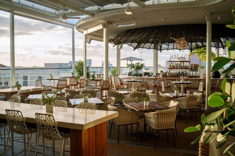Rooftop bar and lounge with waterfront views, woven chairs, white bar counter, and potted plants