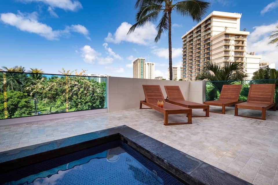 Rooftop terrace with wooden loungers, spa pool, palm trees, and high-rise residential views