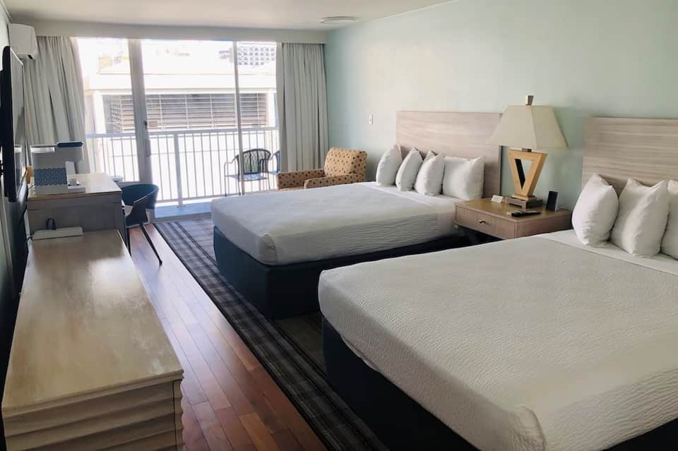 Hotel room with twin beds, ocean balcony view, light blue walls, and modern furnishings