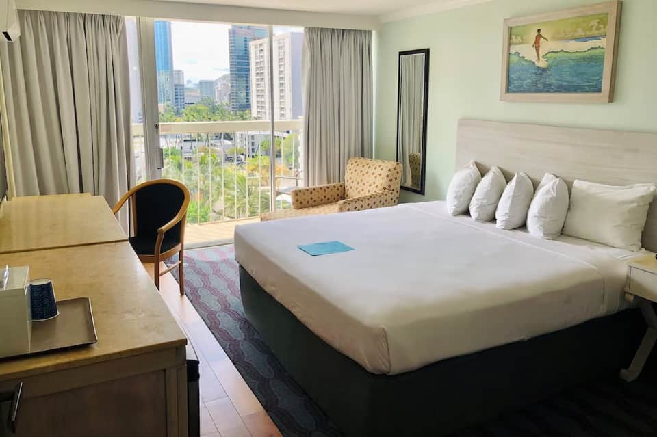 Hotel room with king bed, balcony overlooking city skyline, and light green walls