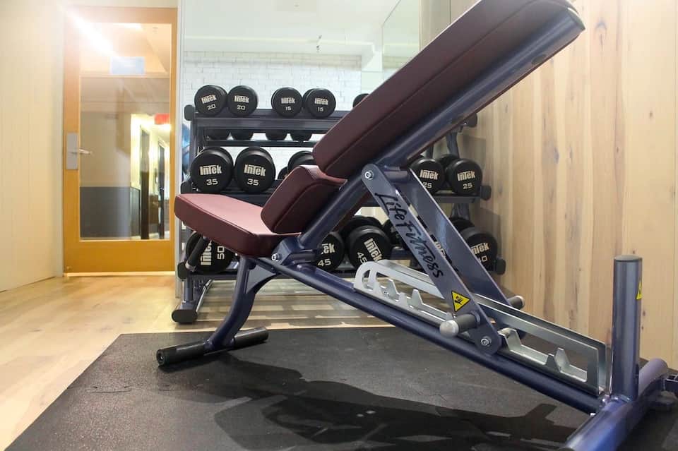 Fitness center featuring weight bench and dumbbell rack with mirrors and wooden flooring