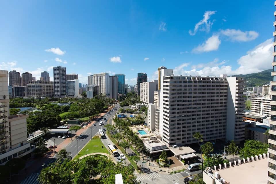 Aerial cityscape view of Honolulu with high-rise hotels, green parks, and mountains in background