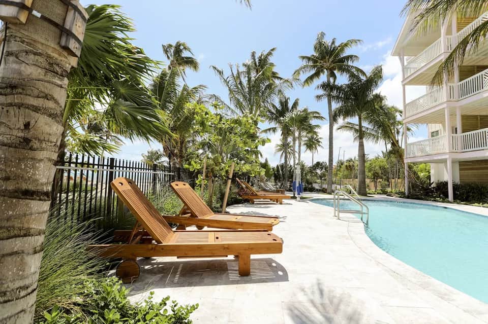 Resort pool deck with wooden lounge chairs, palm trees, and multi-story hotel building