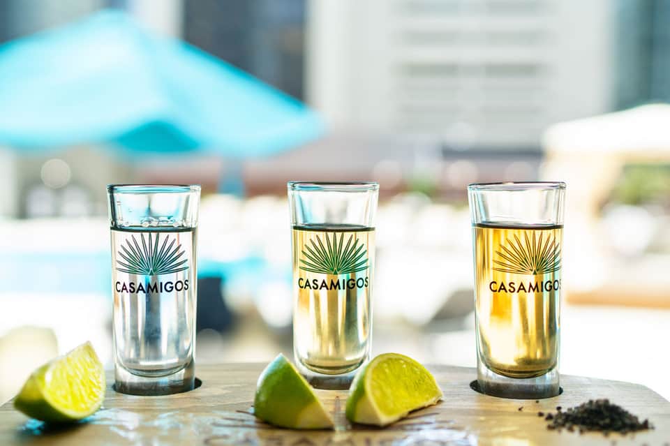 Three Casamigos tequila shots with lime wedges on a poolside table