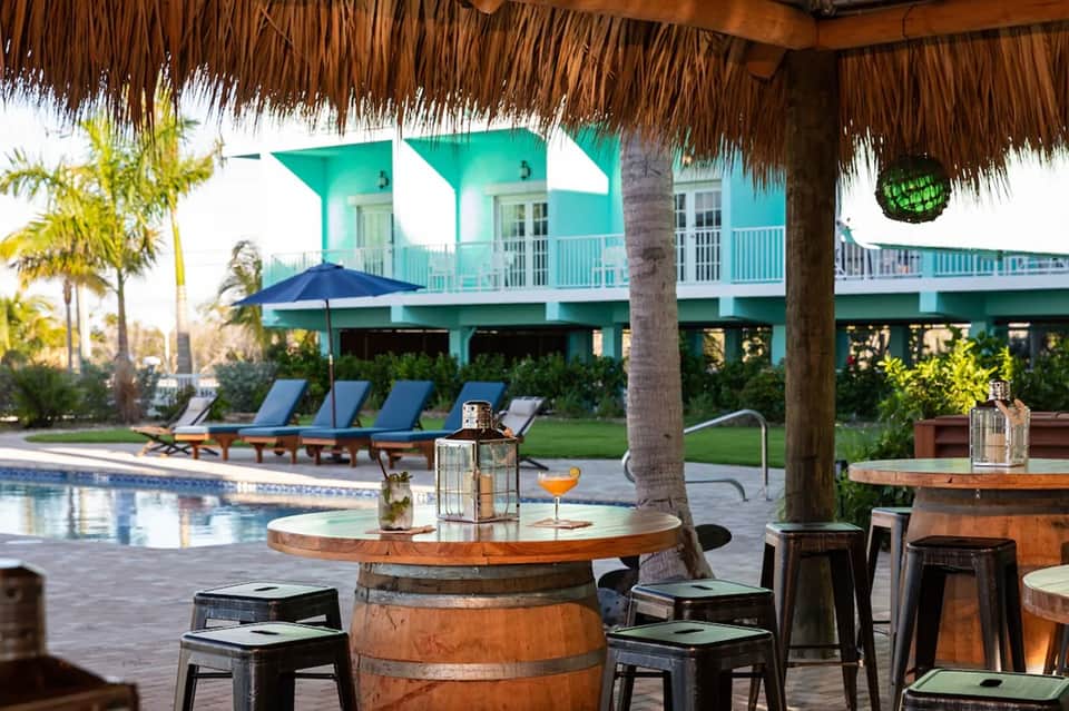 Turquoise tropical home with pool, lounge chairs, thatched bar structure, and manicured lawn
