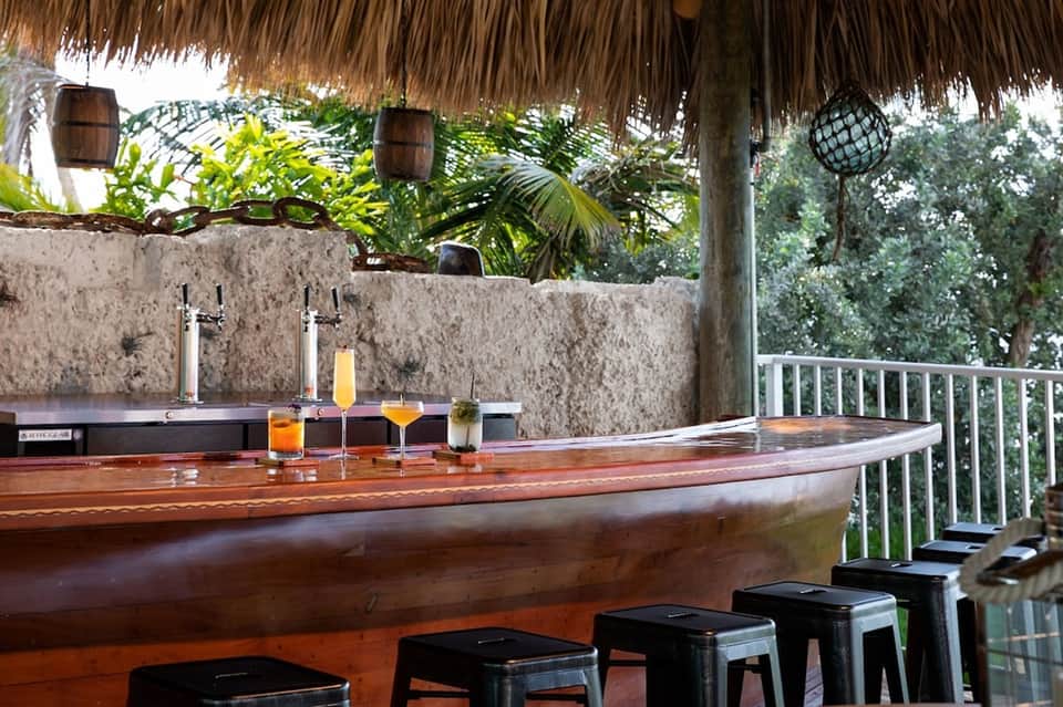 Thatched-roof tropical bar with wooden counter, stone wall, and oceanfront railing