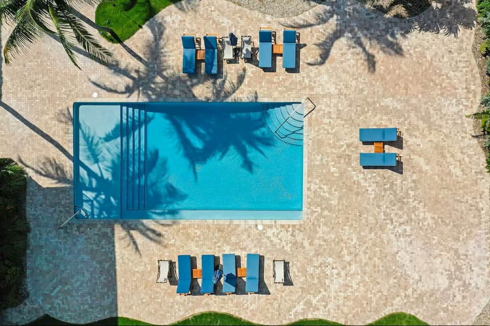 Overhead view of small pool with blue loungers and palm shadows on paved deck