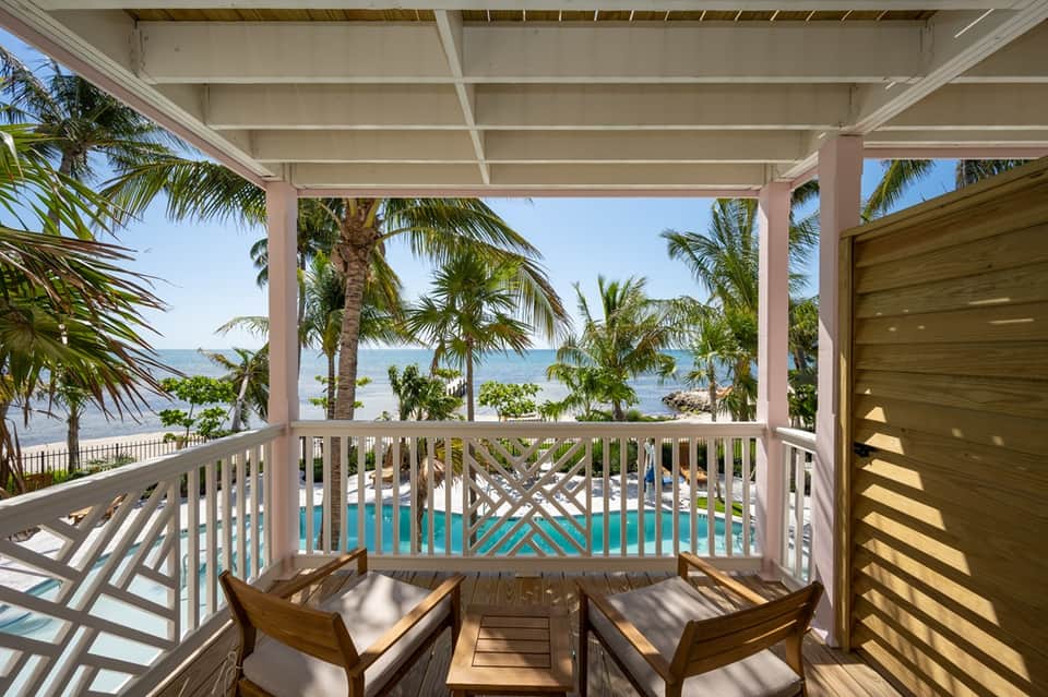 Beachfront covered deck with lounge chairs overlooking ocean, palm trees, and pool