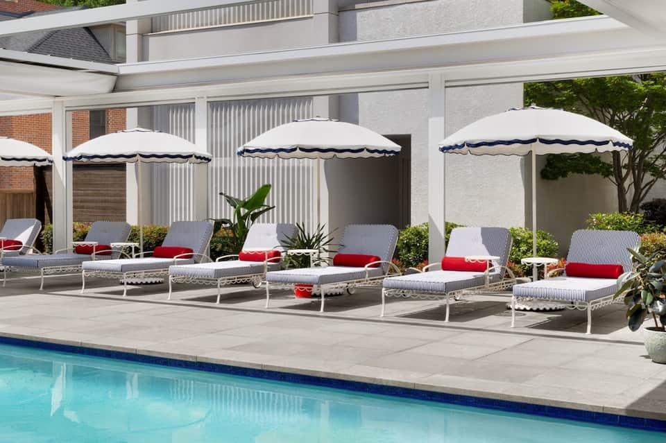 Poolside lounge area with striped chaise lounges, white scalloped umbrellas, and green landscaping