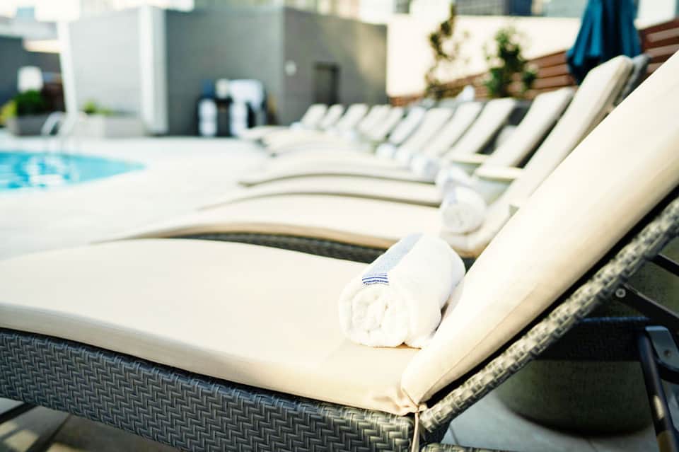 Row of white lounge chairs with rolled towels beside an outdoor swimming pool