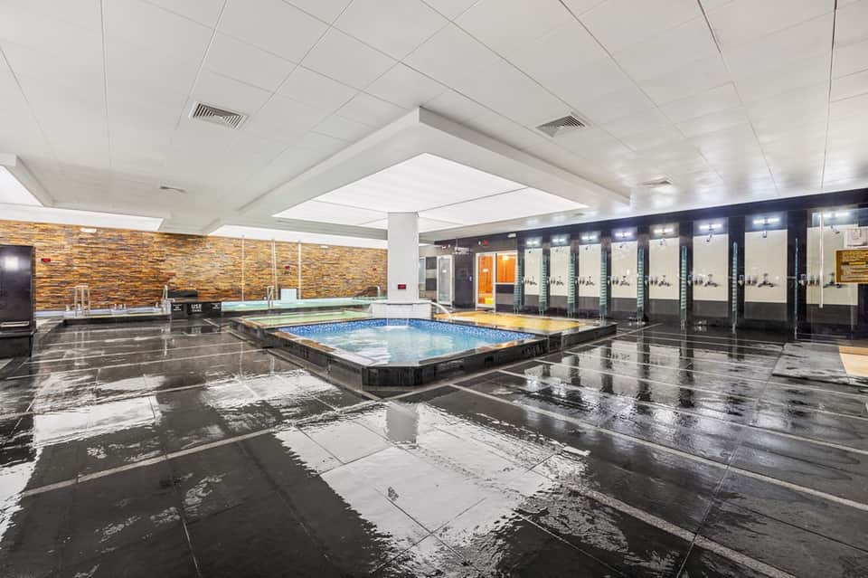 Modern indoor swimming pool with sleek design, skylights, spa area, and mirrored glass walls