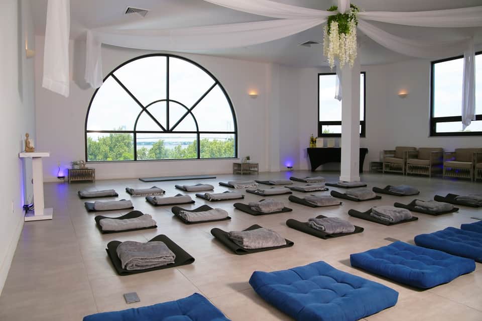 Meditation or yoga studio with arched windows, rolled yoga mats on floor, blue cushions, and scenic landscape view