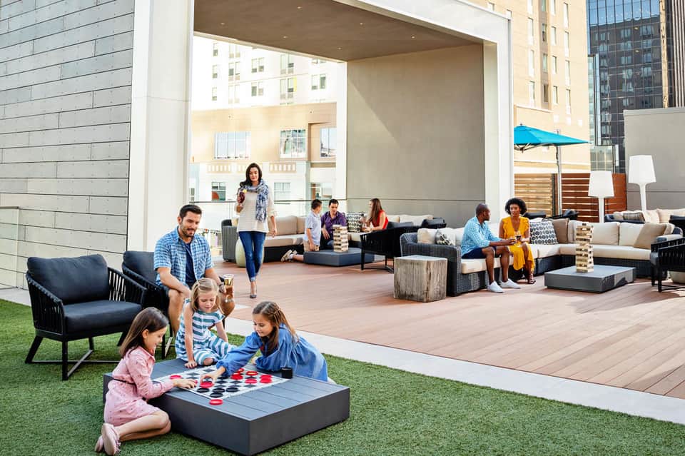 Rooftop terrace with families playing games, lounge seating, and city views with modern architecture
