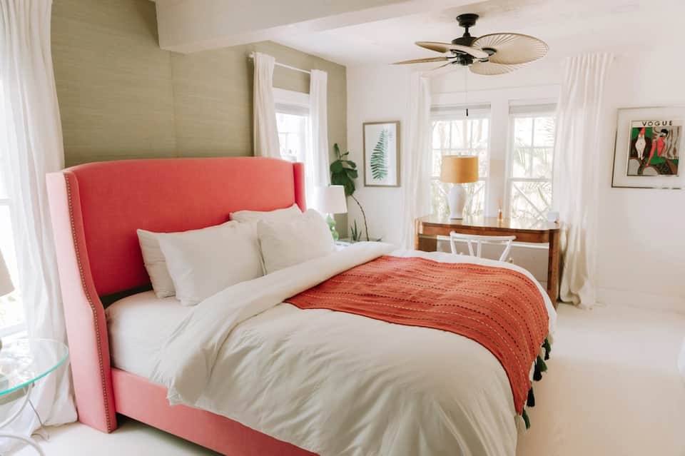 Bright bedroom with coral headboard, white bedding, ceiling fan, and garden views