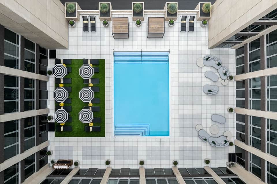 Overhead view of hotel courtyard with rectangular blue pool, striped umbrellas, and surrounding apartments