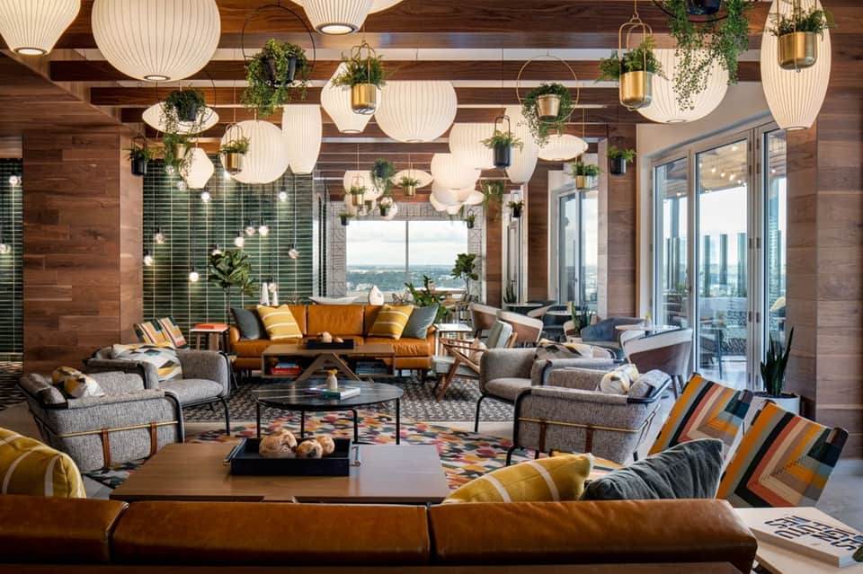 Modern hotel lounge with hanging pendant lights, wood ceiling, colorful seating, and floor-to-ceiling windows