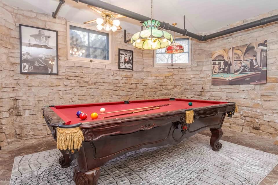 Game room with ornate pool table, red felt, stone walls, stained glass pendant lights, and vintage photographs