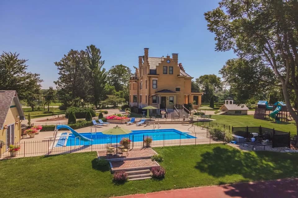 Historic mansion with pool, slide, and manicured lawn surrounded by trees and playground equipment