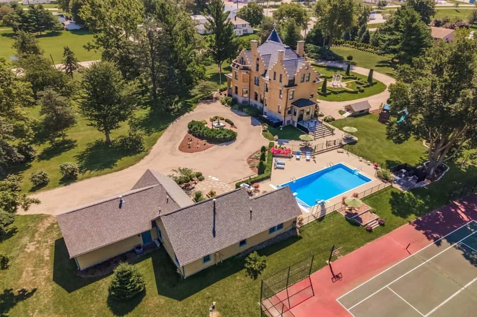 Aerial view of estate with castle-like mansion, swimming pool, sports courts, and manicured grounds