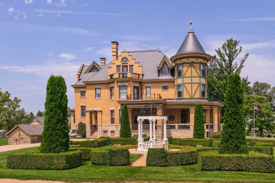 Historic yellow Victorian mansion with turret, manicured gardens, and gazebo