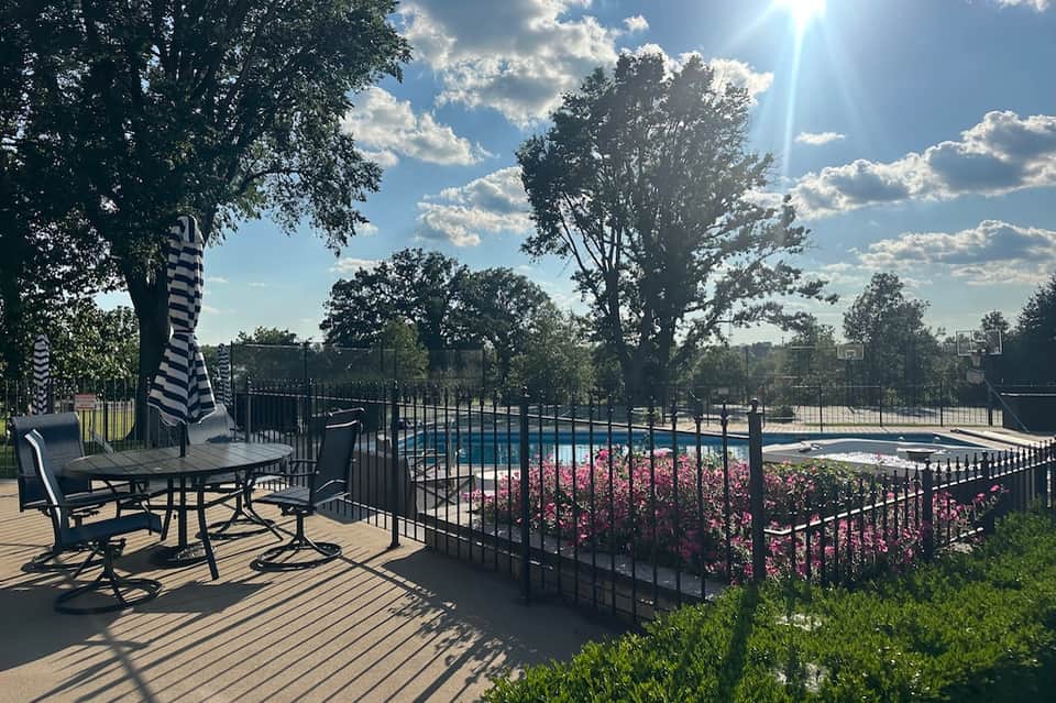 Residential pool deck with black railing, striped umbrella, lounge seating, and sports court