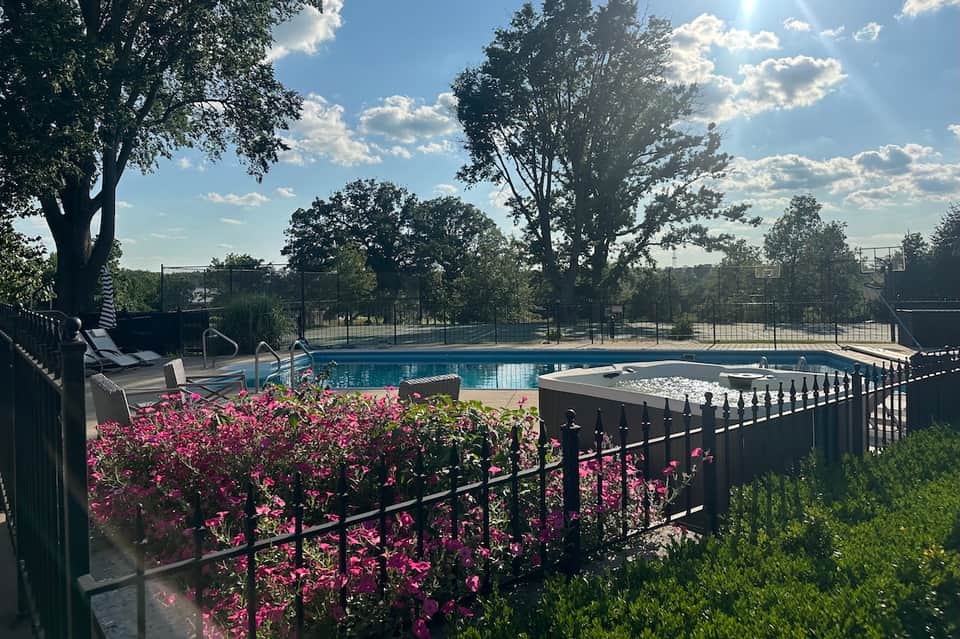 Resort pool with lounge chairs, spa hot tub, pink flowering plants, and tree-lined surroundings