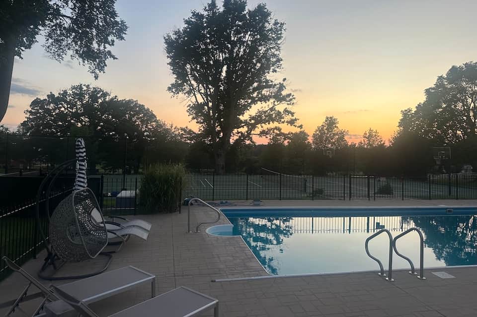 Resort swimming pool at dusk with lounge chairs, fire pit, and scenic natural surroundings