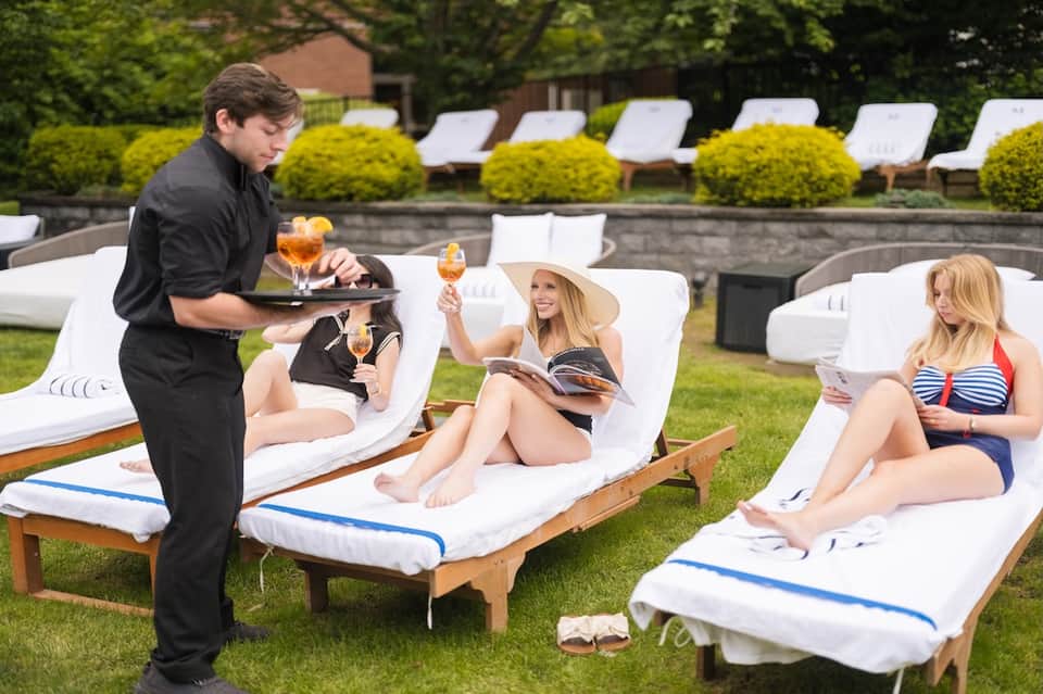 Guests enjoying beverages on lounge chairs by poolside grass area during daytime service