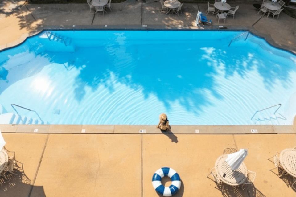Overhead view of swimming pool with person standing on deck, umbrellas, and lounge chairs casting shadows