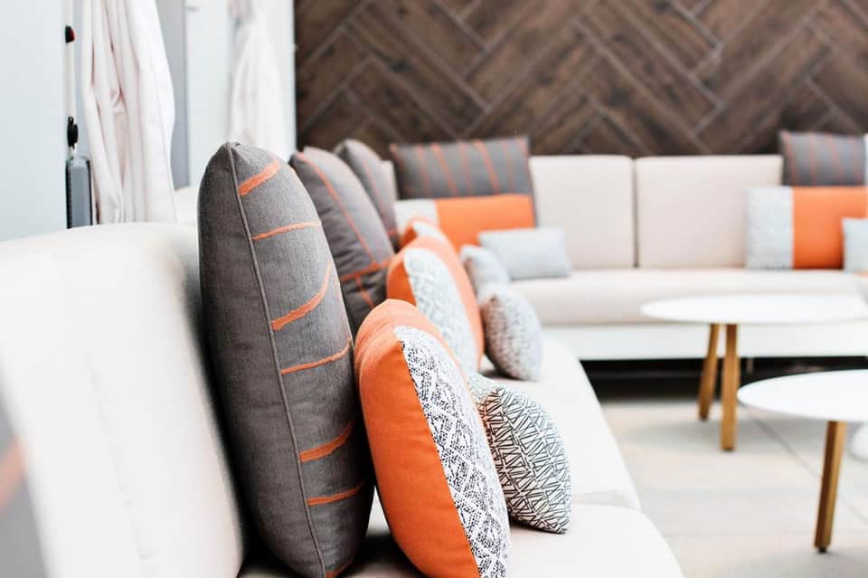 Display of decorative pillows in gray, orange, and patterned designs on white seating furniture