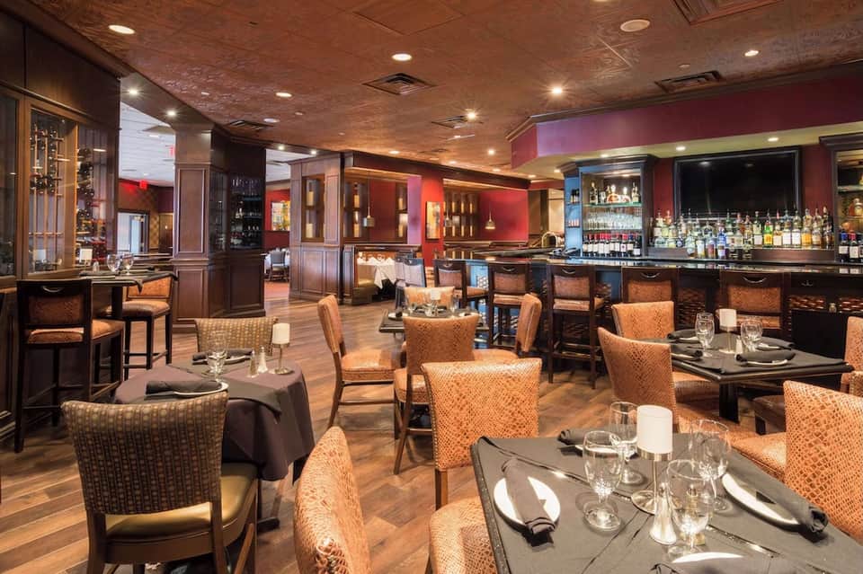 Upscale restaurant and bar with orange chairs, wood paneling, ambient lighting, and full bar