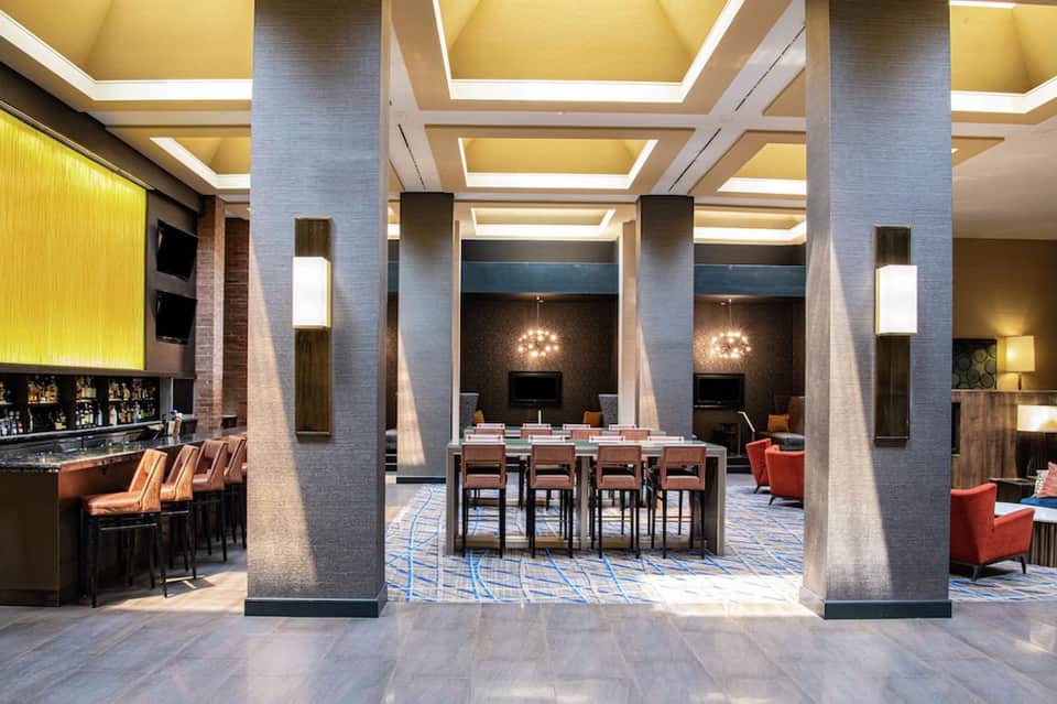 Modern hotel lobby with geometric ceiling design, bar seating, and contemporary furnishings