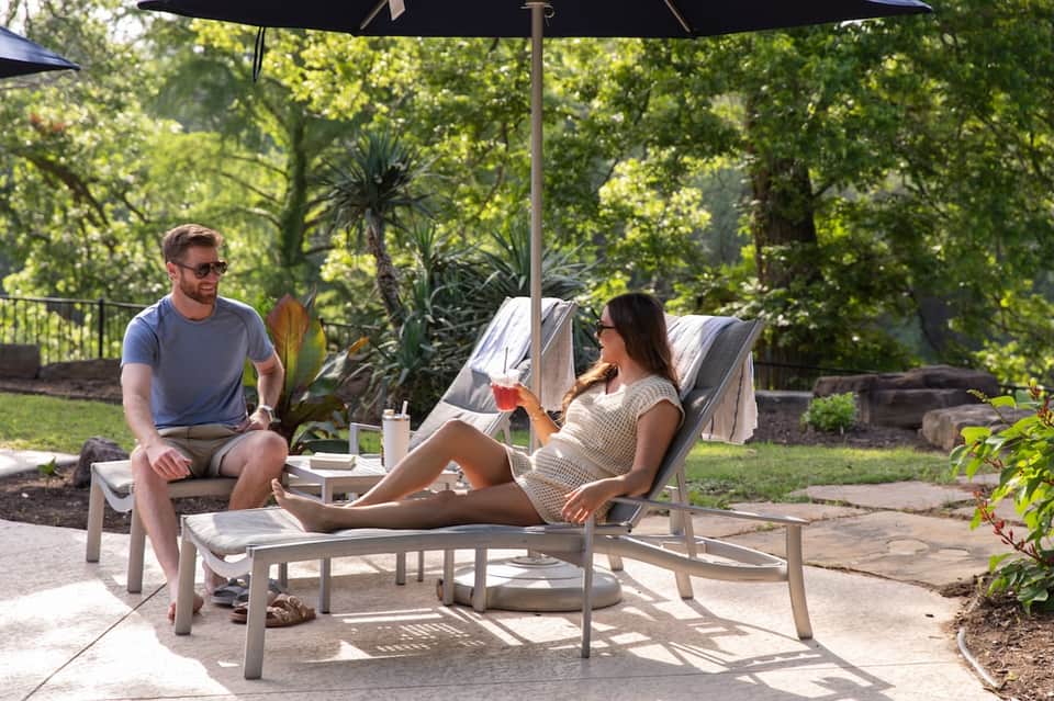 Couple relaxing on lounge chairs under black umbrella in landscaped garden setting