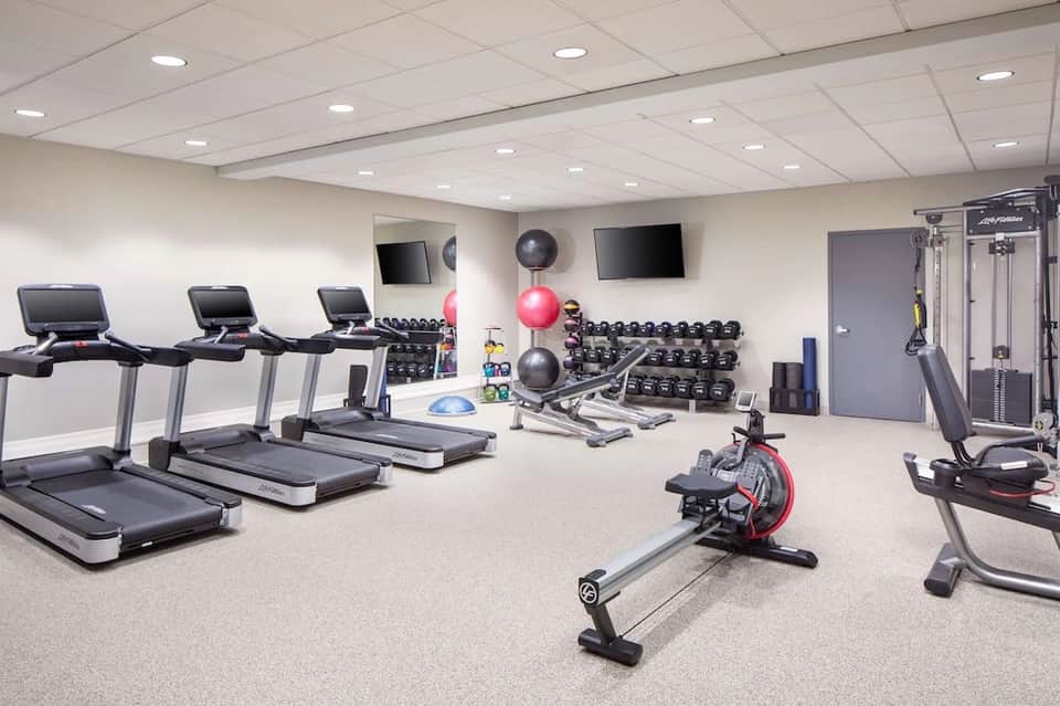 Modern fitness center with treadmills, dumbbells, exercise bikes, and TV screens