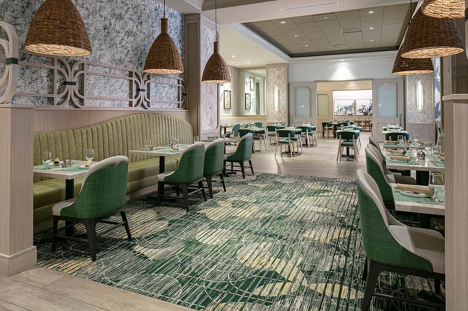 Upscale hotel restaurant with green banquette seating, pendant lights, and refined decor