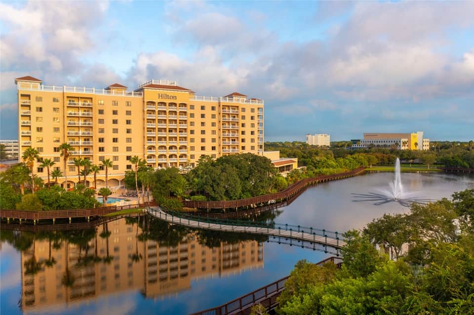 Yellow Hilton resort building reflected in still water with fountain and landscaped grounds