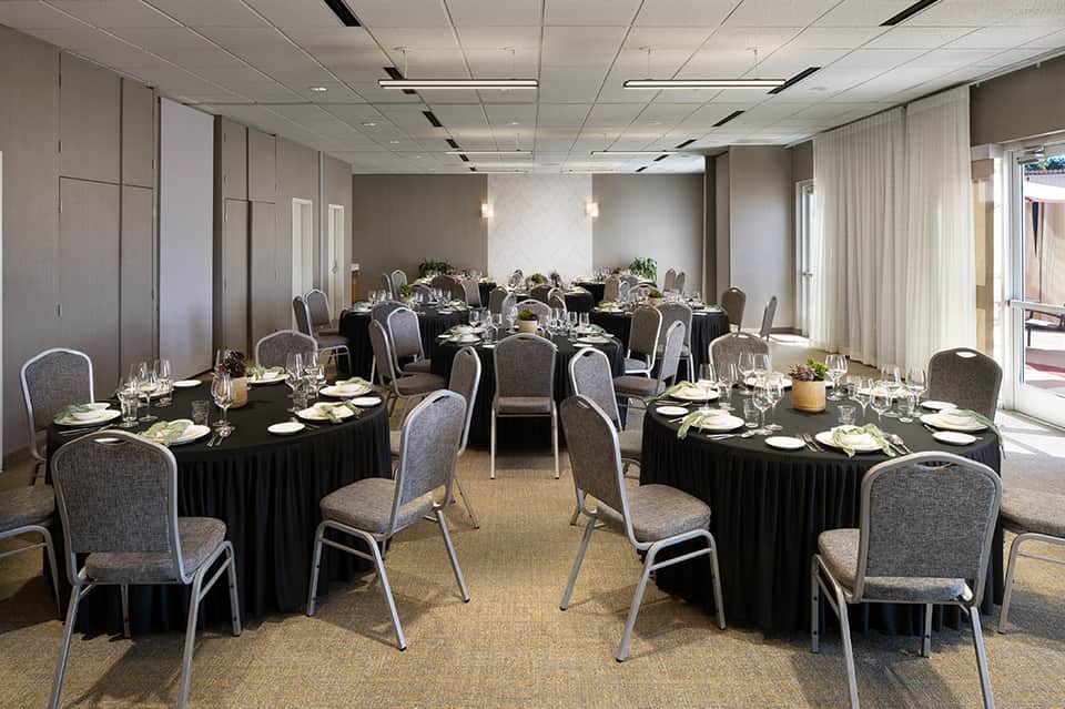 Elegant ballroom with round tables set with black linens, gray chairs, and natural light from floor-to-ceiling windows