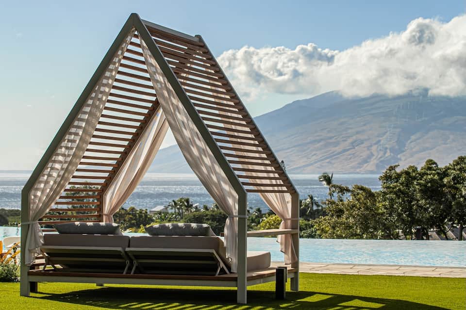 Modern cabana with striped shade structure overlooking infinity pool and mountain lake landscape