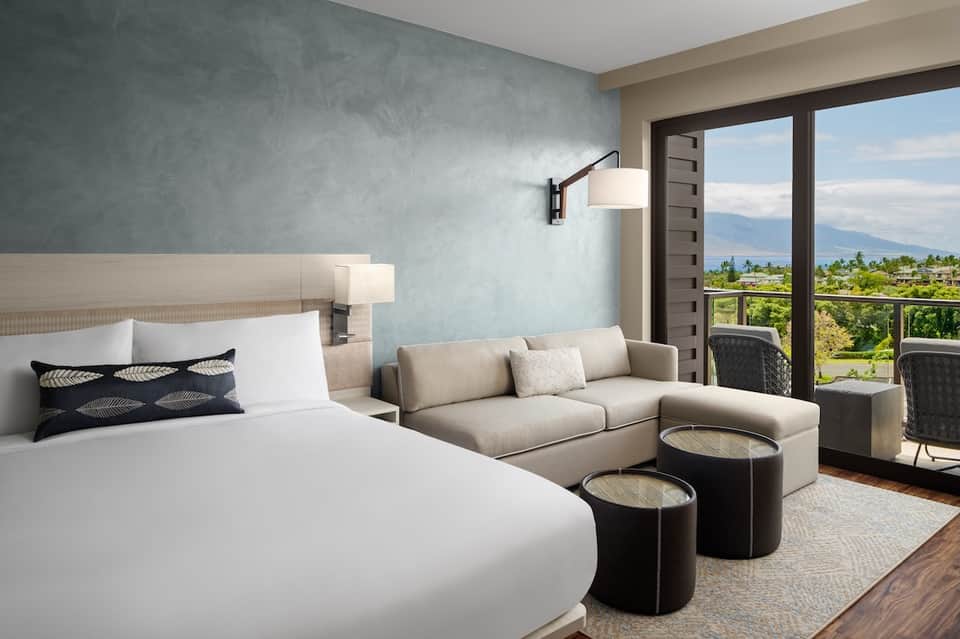 Modern hotel room with bed, sofa, mountain view balcony, and contemporary minimalist design