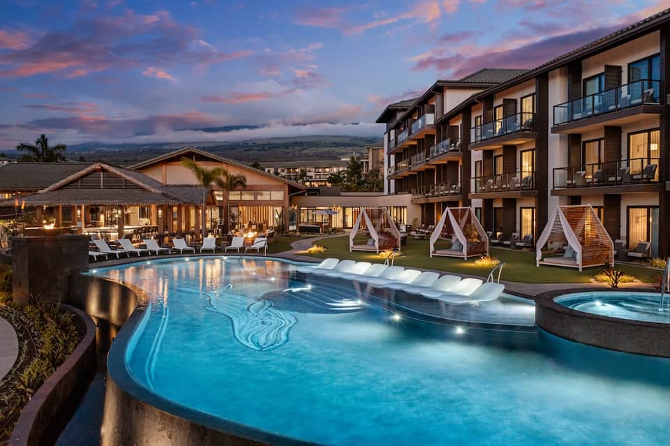 Resort pool complex at sunset with white cabanas, lounge chairs, and mountain valley views